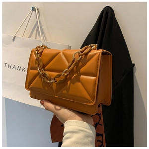 Close-up of orange quilted chain bag with triangle pattern and chunky link strap