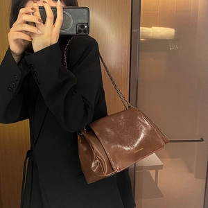 Gros plan d'un sac bandoulière en cuir marron brillant avec bandoulière chaîne et rabat