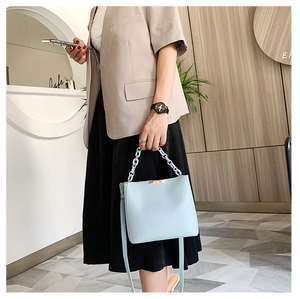 Close-up of a light blue bucket bag with a chain handle held by a model in a beige suit