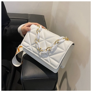 Detail of white quilted crossbody bag with chunky gold chain and patterned strap
