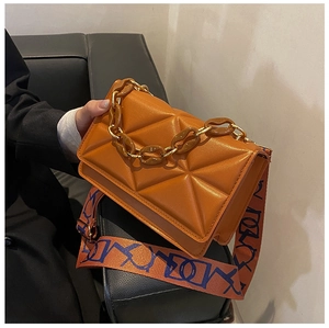 Detail of orange quilted crossbody bag with amber resin chain and abstract strap