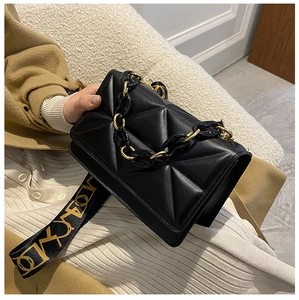 Detail of black quilted leather crossbody bag with chain handle and wide fabric strap