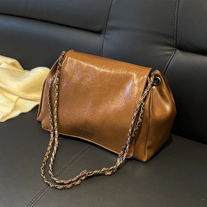 Sac bandoulière rétro marron caramel plissé avec chaîne sur un canapé en cuir