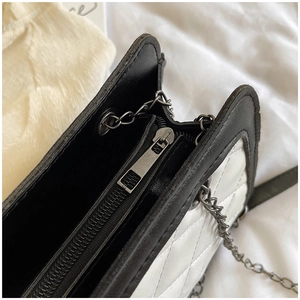 Detail of quilted rhombus bag with black and white contrast stitching and metal chain