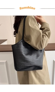 Side view of large black hand-woven shoulder tote bag worn by a model in a minimalist room