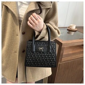 Détail du sac bandoulière matelassé noir avec nœud doré et poignée sur le dessus