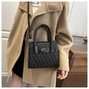 Sac à main noir matelassé avec nœud doré présenté sur un manteau texturé