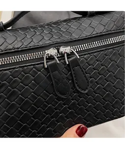 Detail of black woven leather handbag showing dual metal zippers and long leather pulls
