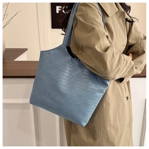 Close-up side view of light blue woven tote bag held by a model in a trench coat