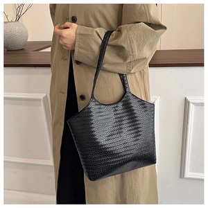 Detail of black woven leather tote bag texture on a stylish woman in a trench coat
