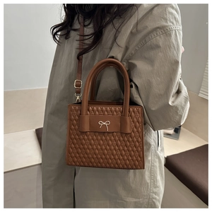Vue détaillée du sac matelassé marron caramel avec nœud doré et deux poignées de transport
