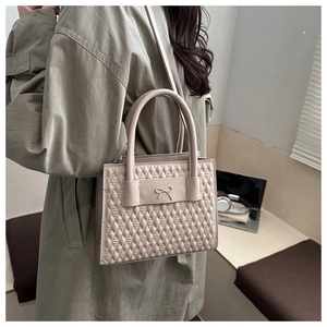 Detail of a beige quilted tote bag with metal bow and cylindrical handles worn by model