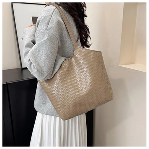 Detail of a large khaki woven tote bag showing texture and shoulder strap fit on a model