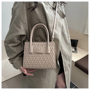 Gros plan du sac beige matelassé avec nœud métallique décoratif et poignée ronde