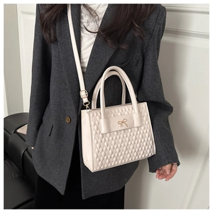 Detail of cream quilted tote bag featuring a metallic bow and adjustable shoulder strap