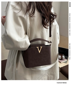 Detail of a brown textured leather crossbody bag with a gold V buckle and shoulder strap