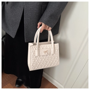 Close-up of cream tote bag with quilted diamond pattern and metal bow decoration