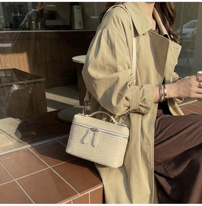 Cream woven texture crossbody vanity bag worn over a trench coat in city setting
