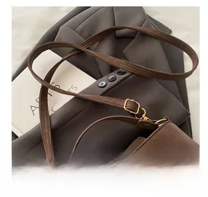 Detail of adjustable shoulder strap and golden V-shaped logo on brown vintage leather bag
