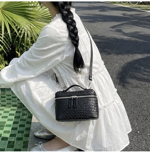 Detail of black woven texture vanity box bag with silver zipper and chain strap