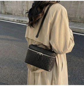 Outdoor street view of a black woven crossbody bag on a beige trench coat