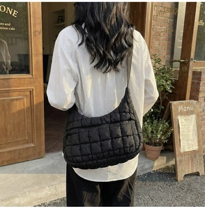 Quilted crossbody bag with a wide fabric strap shown in a stylish cafe setting