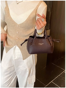 Detail of dark coffee leather handbag featuring pebbled texture and fashion gold lettering
