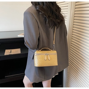 Detail of ginger woven box bag with top handle and fine strap on deep gray suit