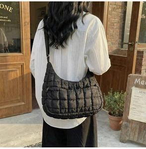 Rear view of a black quilted cloud crossbody bag worn by a model in a cafe setting