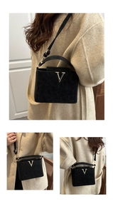 Detail of black suede-textured handbag featuring a signature gold V-shaped metal buckle