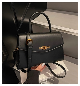 Close-up of black matte shoulder bag featuring a gold clasp and adjustable strap detail