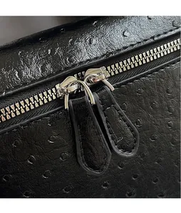 Macro detail of ostrich texture leather and double silver zippers on a black handbag