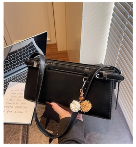 Close-up of minimalist black square shoulder bag with delicate flower charm detail