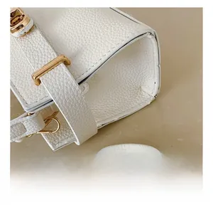 Gros plan sur les coutures du cuir blanc et les ferrures dorées de ce sac minimaliste