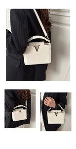 Detailed view of white leather handbag with golden V-shaped logo and metallic hardware