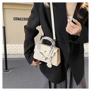 Close-up of cream crocodile pattern bag with silk scarf handle and metal turn-lock clasp