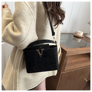 Detail of elegant black crossbody bag with gold V logo shown in a cozy cafe setting
