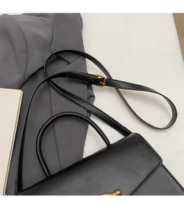 Detail of adjustable leather shoulder strap and handle on a black handbag with gold buckle