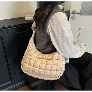 Detail of a beige quilted crossbody bag shown on a model in a minimalist setting