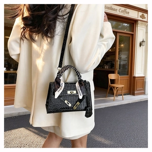 Detail of black crocodile texture handbag with gold buckle and fashion silk scarf wrap