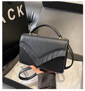 Detail of black textured leather bag with V-shaped flap and elegant metal hardware