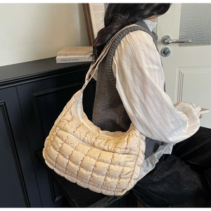 Model wearing a beige quilted crossbody bag with soft padded texture and wide strap