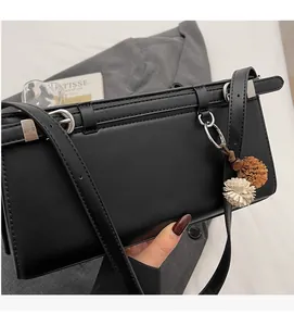 Detail of black rectangular baguette bag with silver buckle and plush pompom accessory