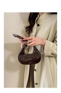 Dettaglio di una borsa a mezzaluna marrone scuro con finitura lucida e hardware oro