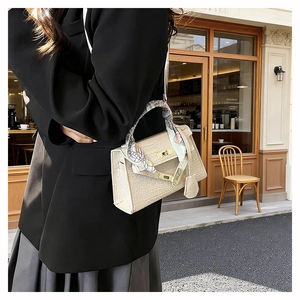 Detailed view of beige crocodile embossed handbag with silk scarf handle and gold buckle