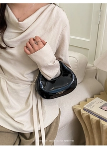 Détail d'un sac demi-lune en cuir verni noir avec texte doré tendance sur le devant