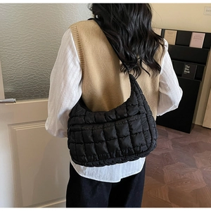 Side view of a black quilted puffer crescent bag worn by a model in a cozy library setting