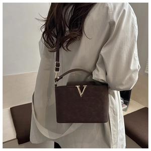 Detail view of dark brown matte leather bag with golden V-shaped metal hardware accessory