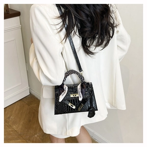 Detail of black crocodile texture handbag with gold lock and decorative silk scarf