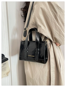 Chic black glossy PU leather handbag worn over the shoulder with gold fashion lettering